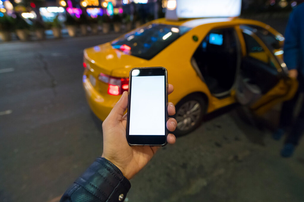 Person Holding Phone Calling For Rideshare With Yellow Car In Background